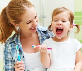 Mom and little girl brushing their teeth and laughing