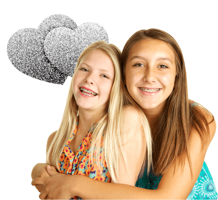 Two teenage girls hugging and smiling with two silver shimmery balloons floating behind them